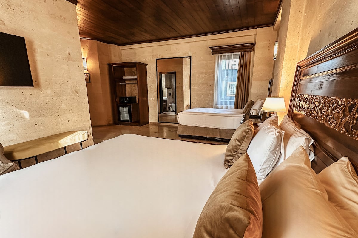 A hotel room with a large bed, a small bedside table, a mirror, and a window with curtains.