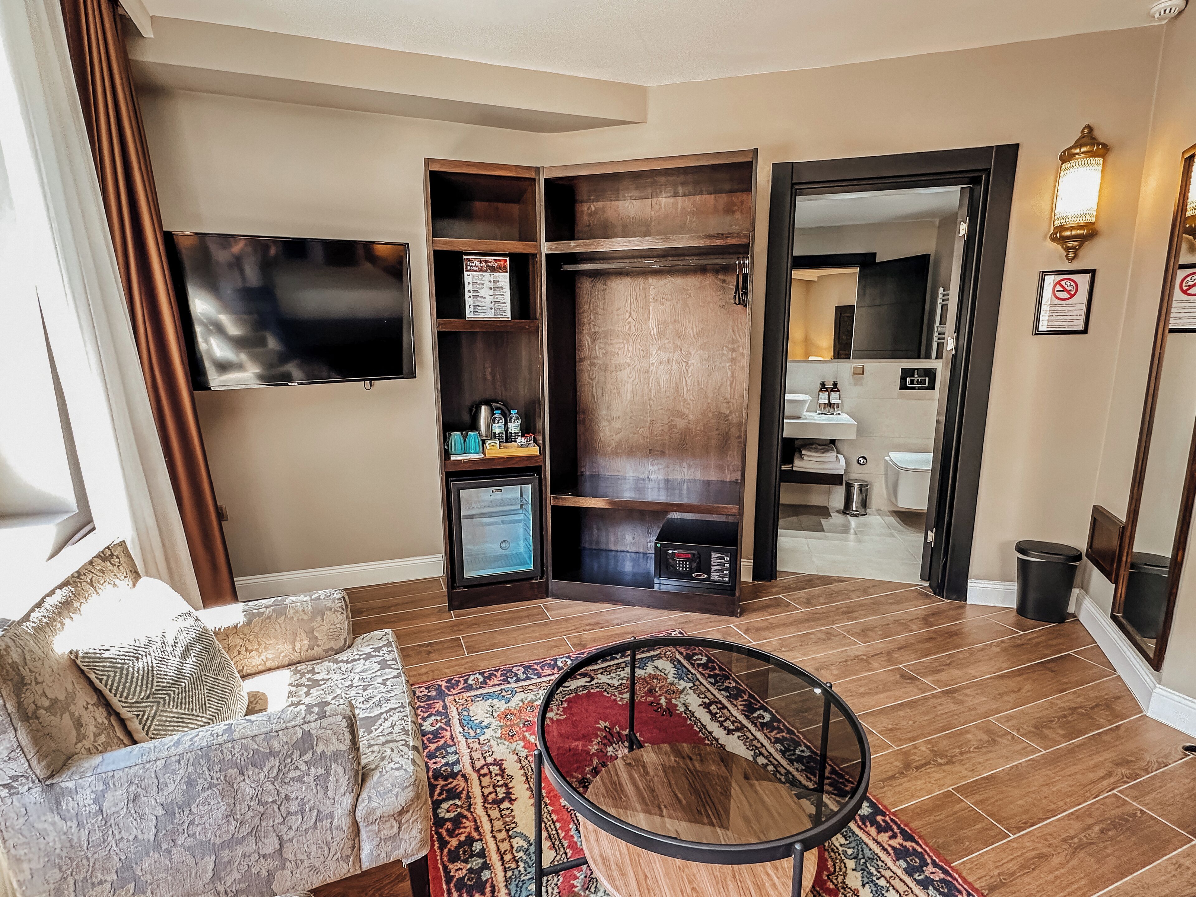 A hotel room with a sofa, a coffee table, a TV, a minibar, and a bathroom visible through an open door.
