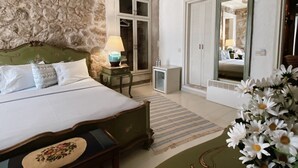 A bedroom with a bed, a nightstand, a lamp, a dresser, a mirror, and a potted plant. - Hoşça kal Alaçatı (Cesme)