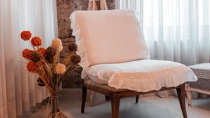 A room with a white chair, a vase with dried flowers, and a stone wall. - Hoşça kal Alaçatı (Cesme)