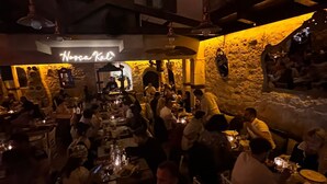 A crowded restaurant with tables and chairs, a neon sign, and stone walls. - Hoşça kal Alaçatı (Cesme)