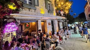 An outdoor dining area with stone walls and a neon sign. - Hoşça kal Alaçatı (Cesme)