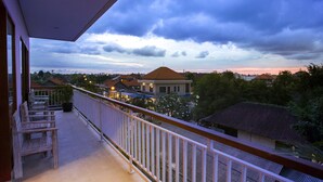 Un balcón con sillas de madera y baranda, con vista a una zona residencial con casas y árboles.