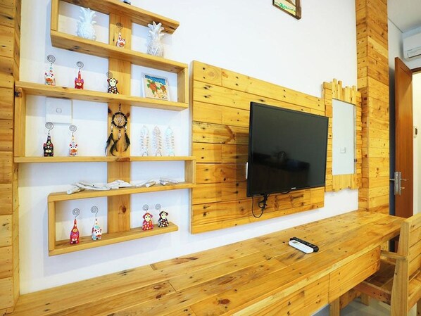 A room with wooden shelves displaying various items, a mounted TV, and a bench.