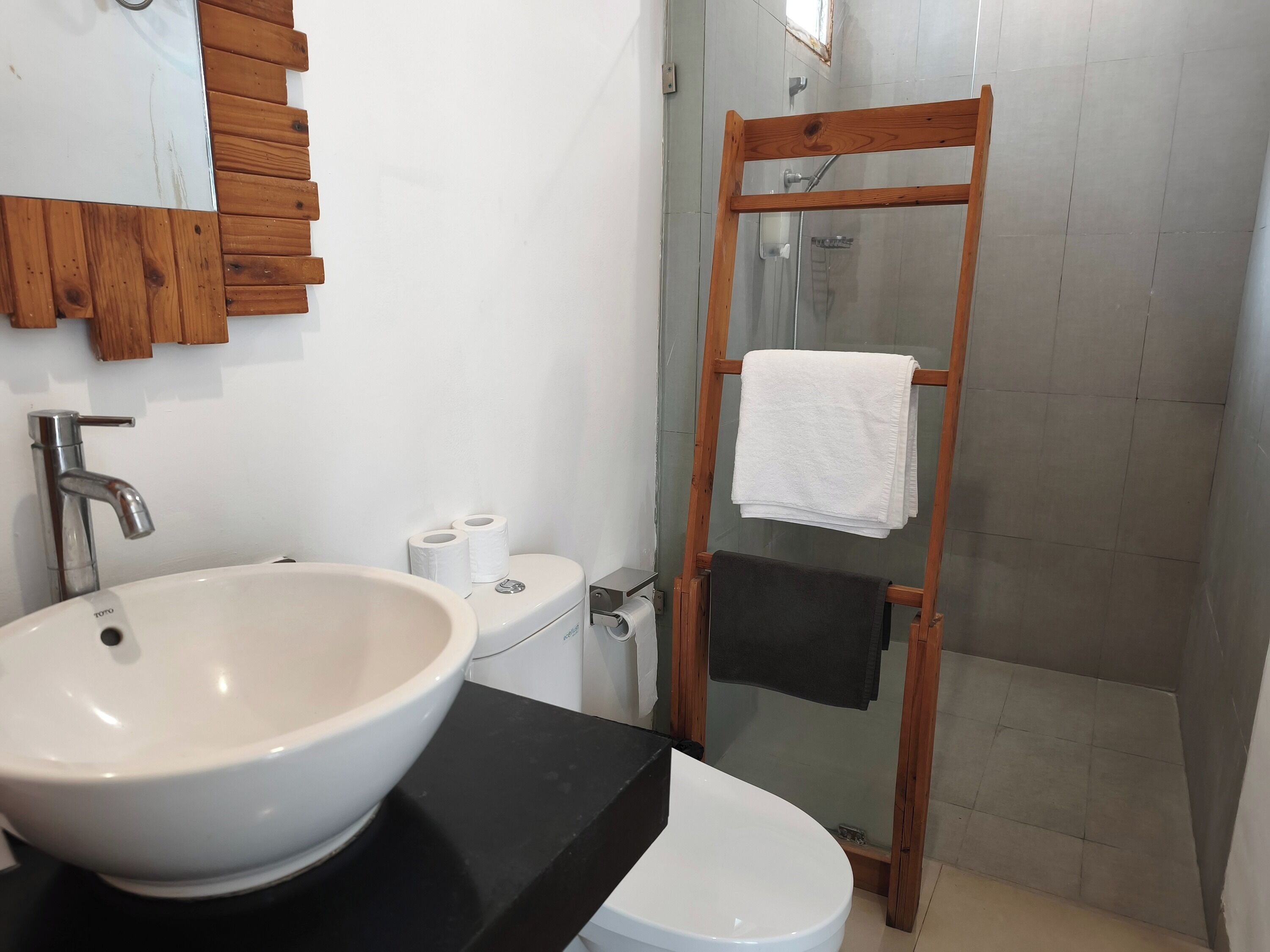 A bathroom with a white sink, toilet, and a wooden towel rack with a white towel.