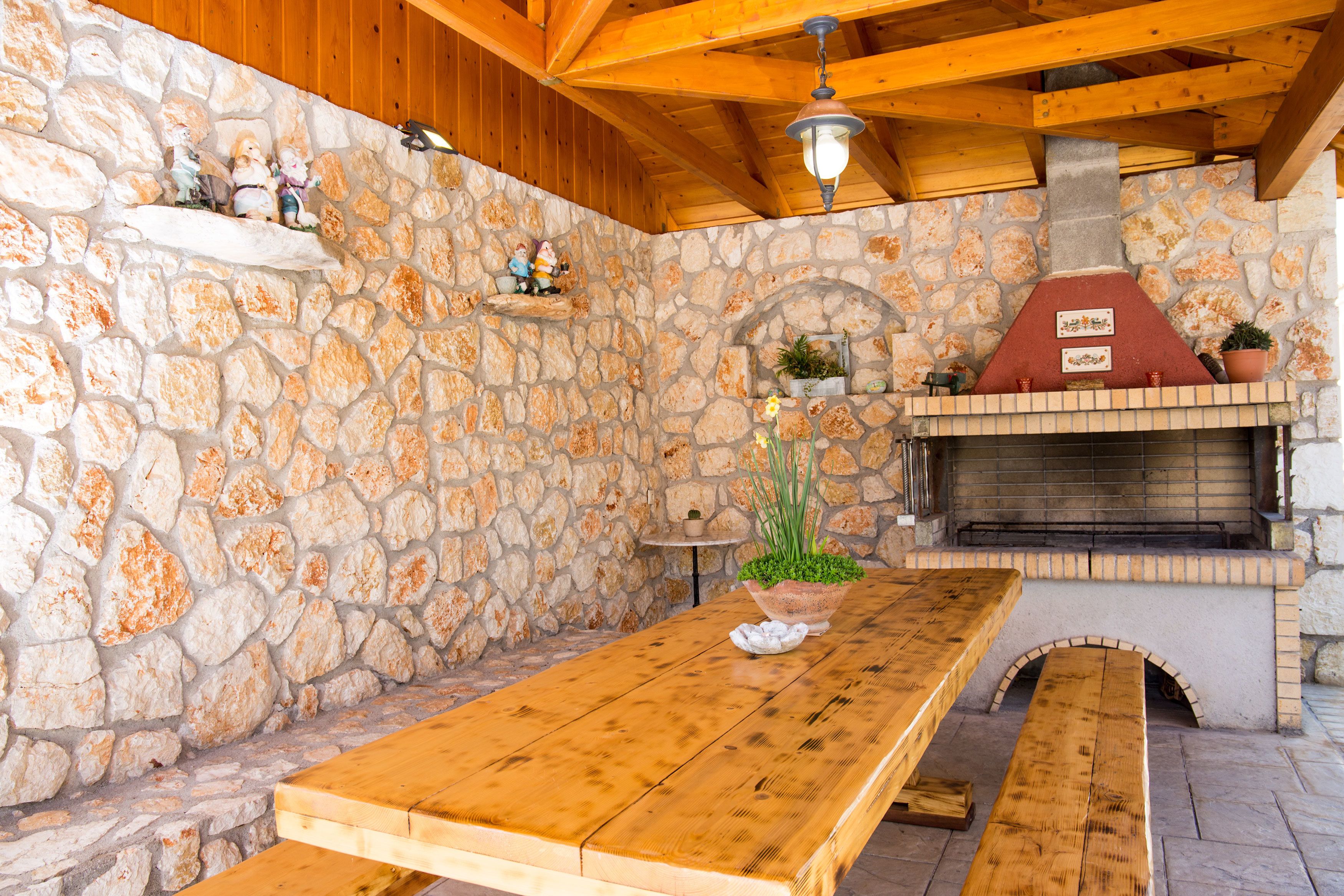 A stone wall with a wooden table and benches, a stone fireplace, and a hanging light fixture.