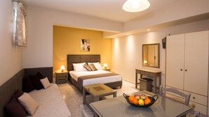 Habitación de hotel con cama, mesita de noche, lámpara y frutero sobre una mesa.