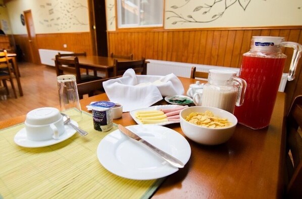 Una presentación de desayuno con una jarra de jugo rojo, un tazón de cereal, un plato con mantequilla, una taza de café y un recipiente de yogur.