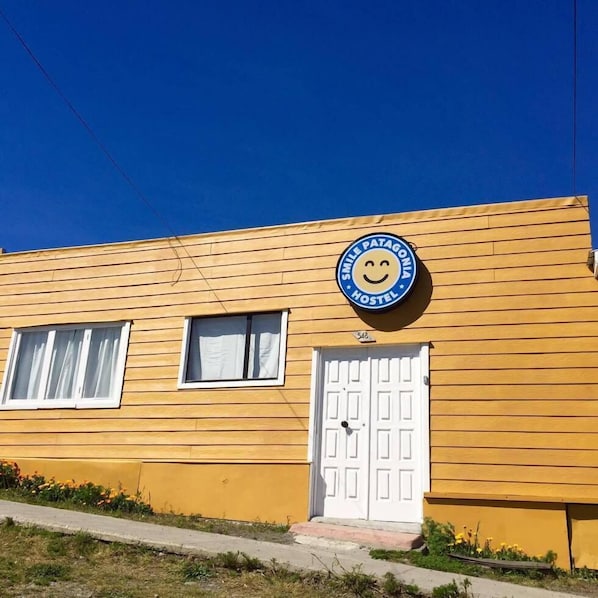 A yellow building with a white door and windows, a blue sign with a smiley face, and the text "SMILE PATAGONIA HOSTEL". - Smile Patagonia Hostel - Adults Only (Natales)