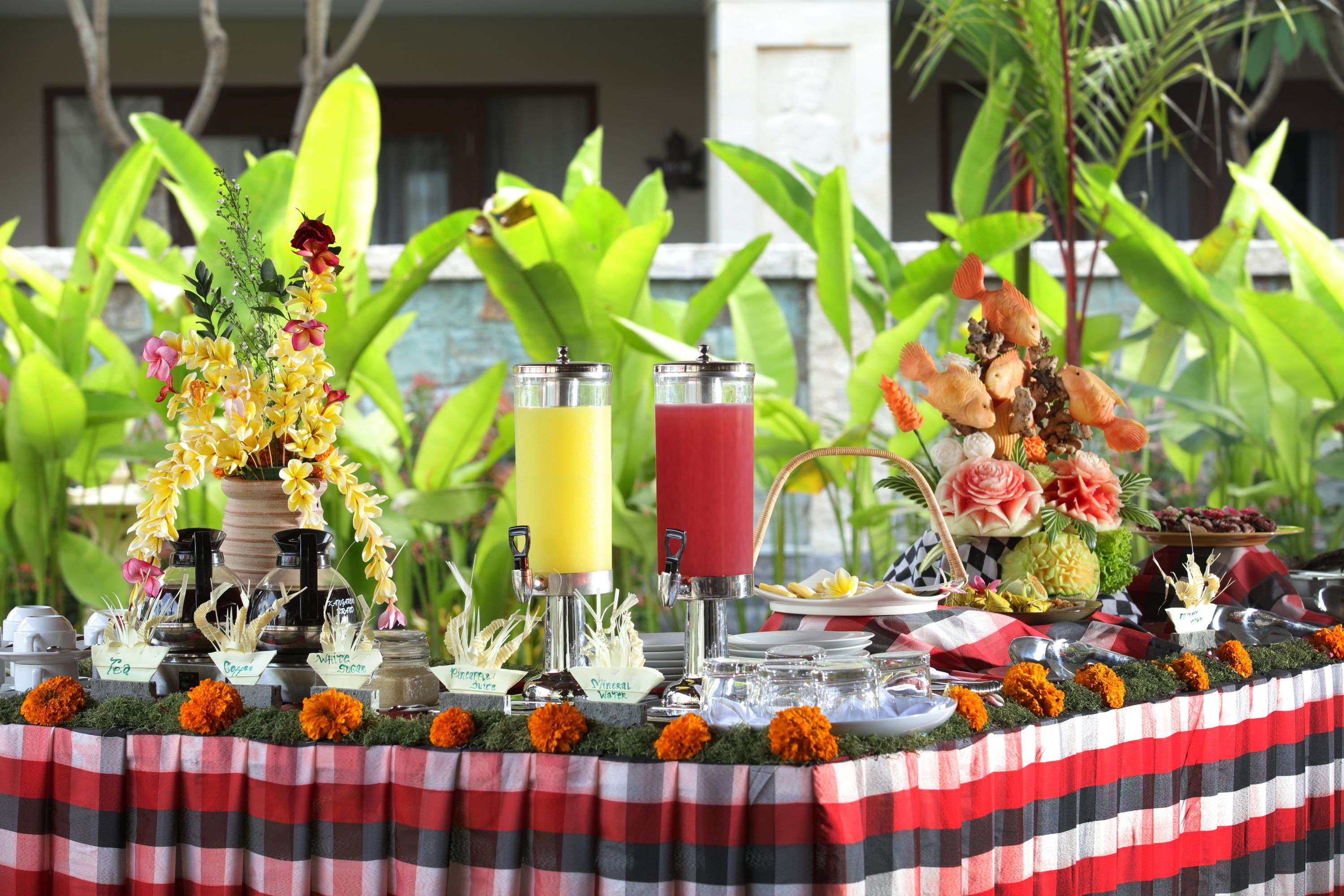 A table set with various drinks, a floral centerpiece, and a tropical backdrop.
