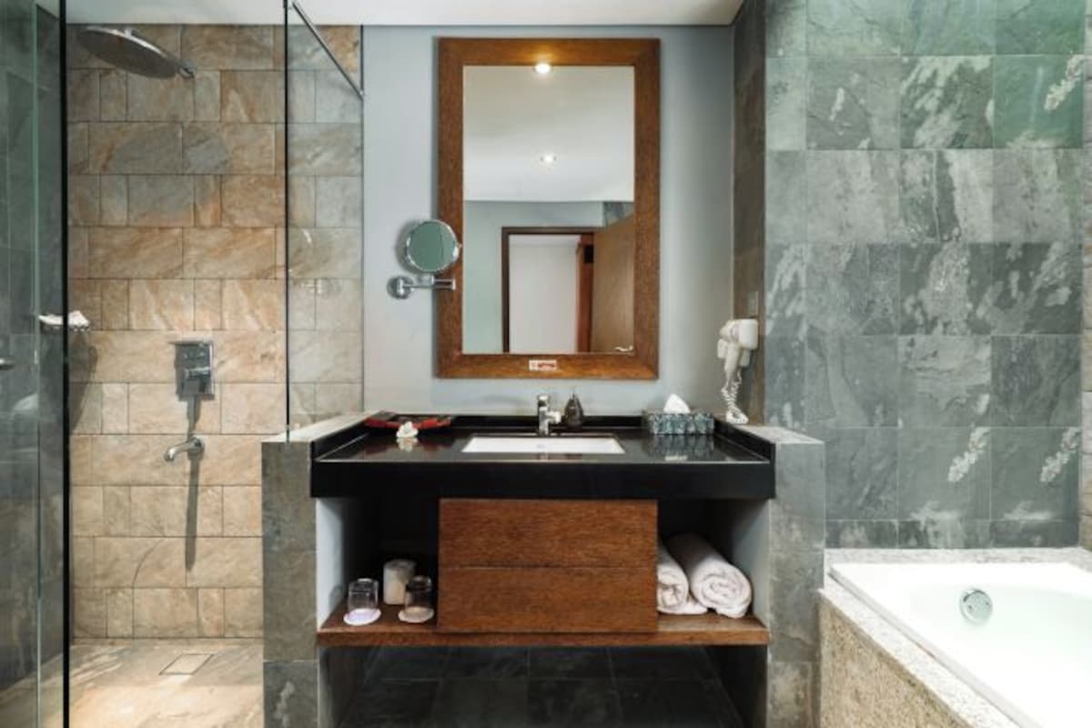 A modern bathroom with a stone shower, a large mirror, a bathtub, and a wooden vanity.