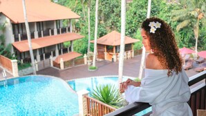 A person in a white robe overlooking a pool area with a building in the background. - Best Western Premier Agung Resort Ubud (Ubud)