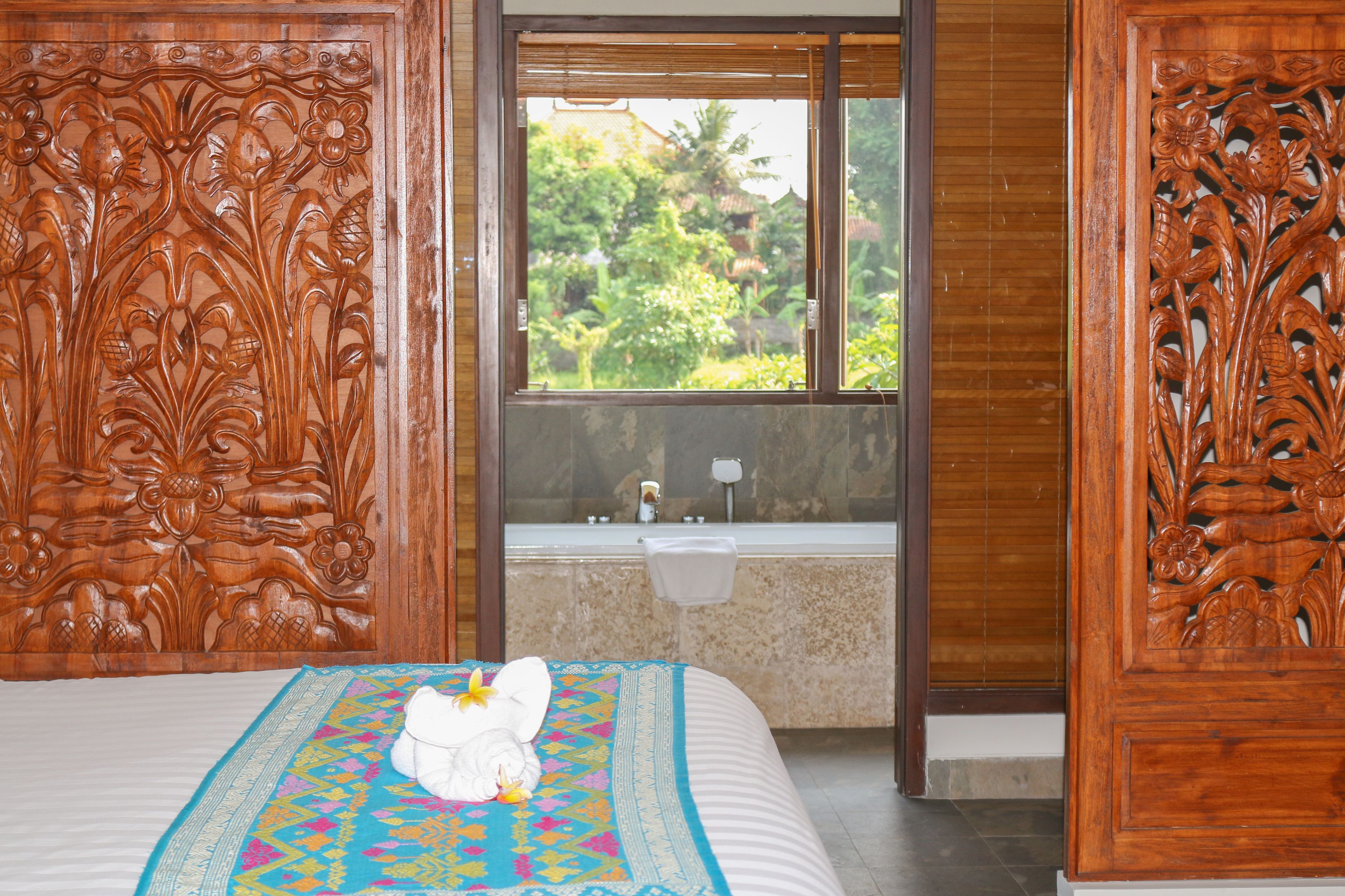 Una habitación con cama, ventana con vista a la vegetación y baño con lavamanos y espejo.