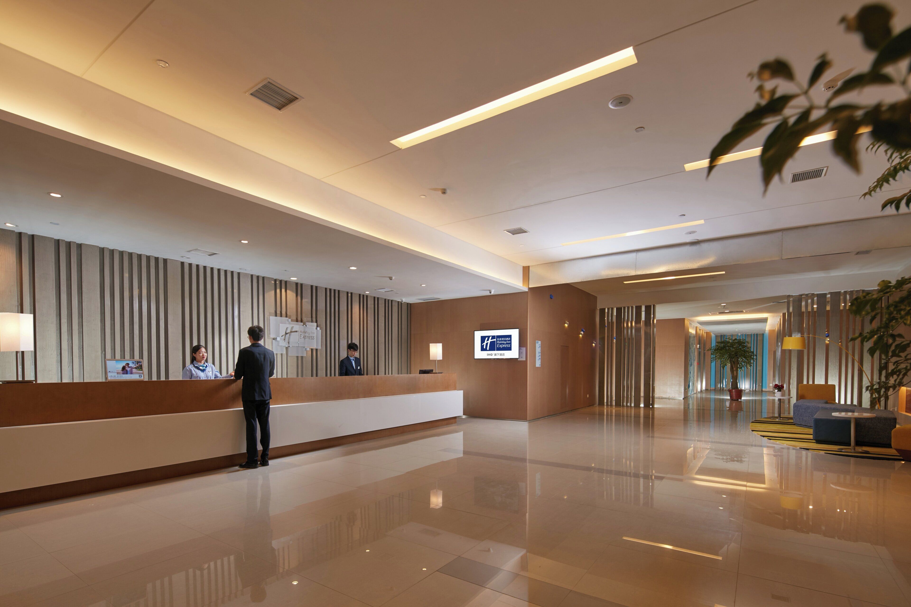 A hotel reception area with a reception desk, a digital screen, and a modern interior design.