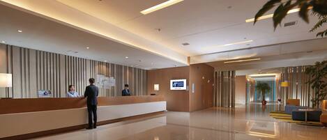 A hotel reception area with a reception desk, a digital screen, and a modern interior design.