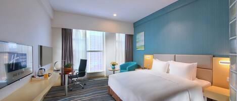 Una habitación de hotel con una cama, un escritorio con silla, un televisor y una ventana con cortinas.