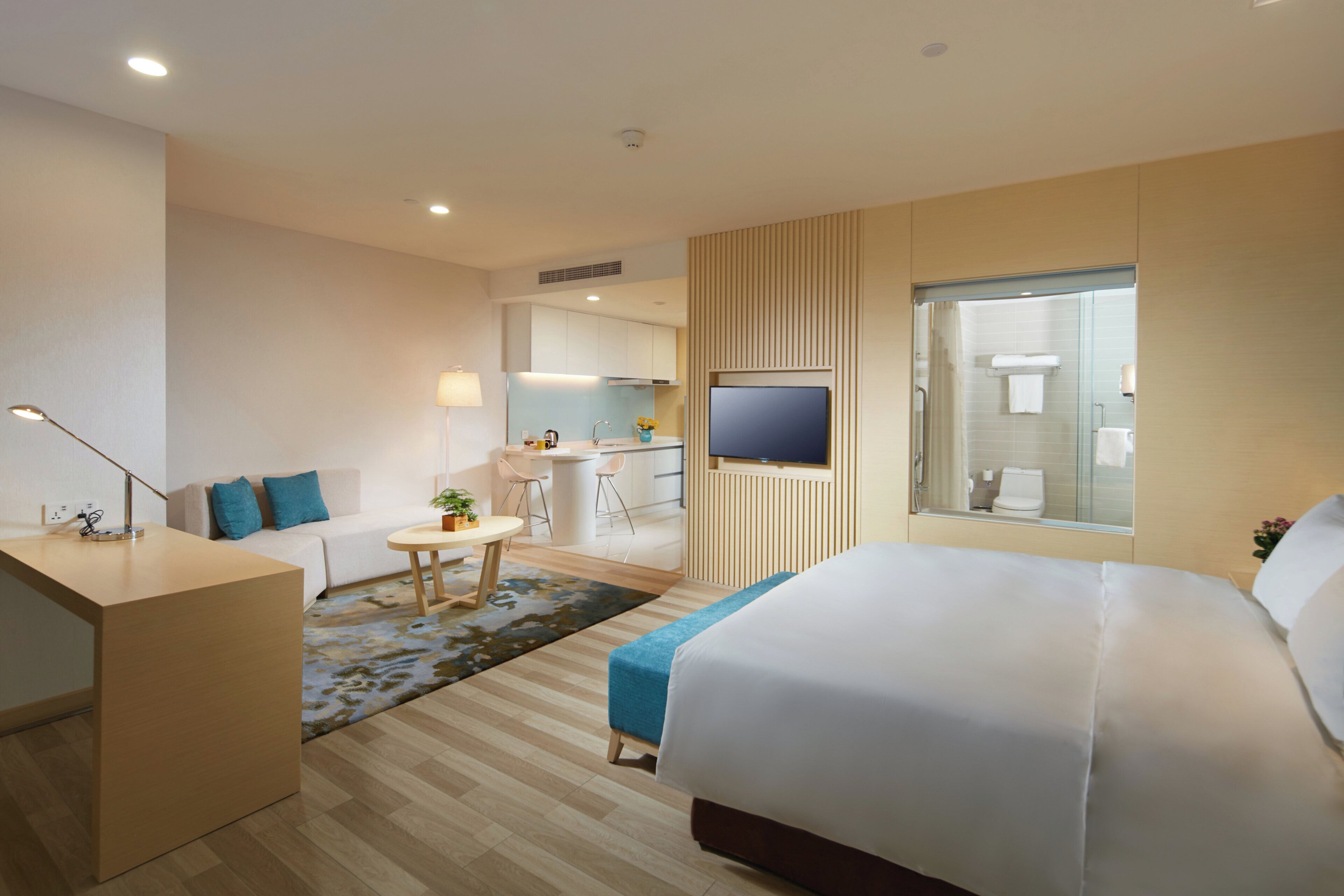A modern hotel room with a bed, a desk, a sofa, a small table, and a TV.