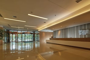 A hotel reception area with a modern design, featuring a reception desk, a large glass door entrance, and a clean, reflective floor. - Holiday Inn Express Luoyang Yichuan by IHG (Luoyang)