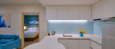 Una cocina moderna con armarios blancos, una isla central con asientos, un horno empotrado y vista a un dormitorio.
