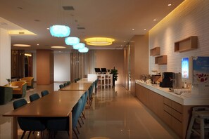 Un moderno hall de hotel con una larga recepción, zona de estar y una barra con máquinas de café.