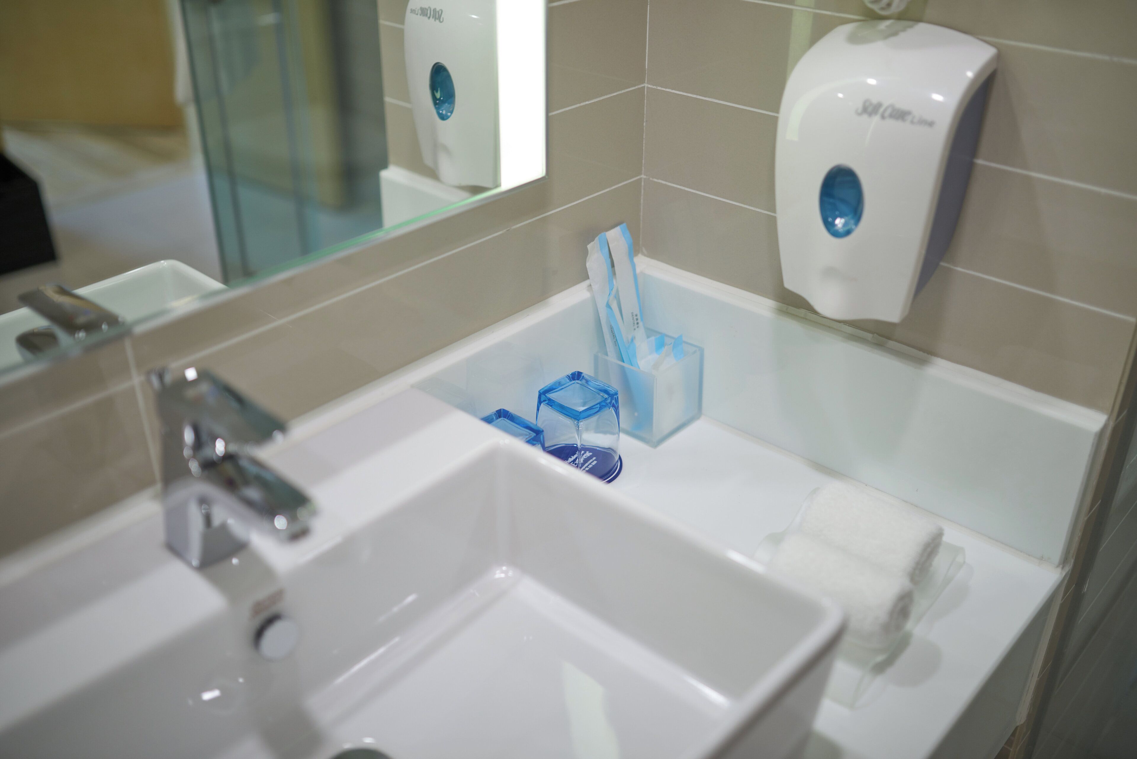 A bathroom with a sink, mirror, and two soap dispensers.
