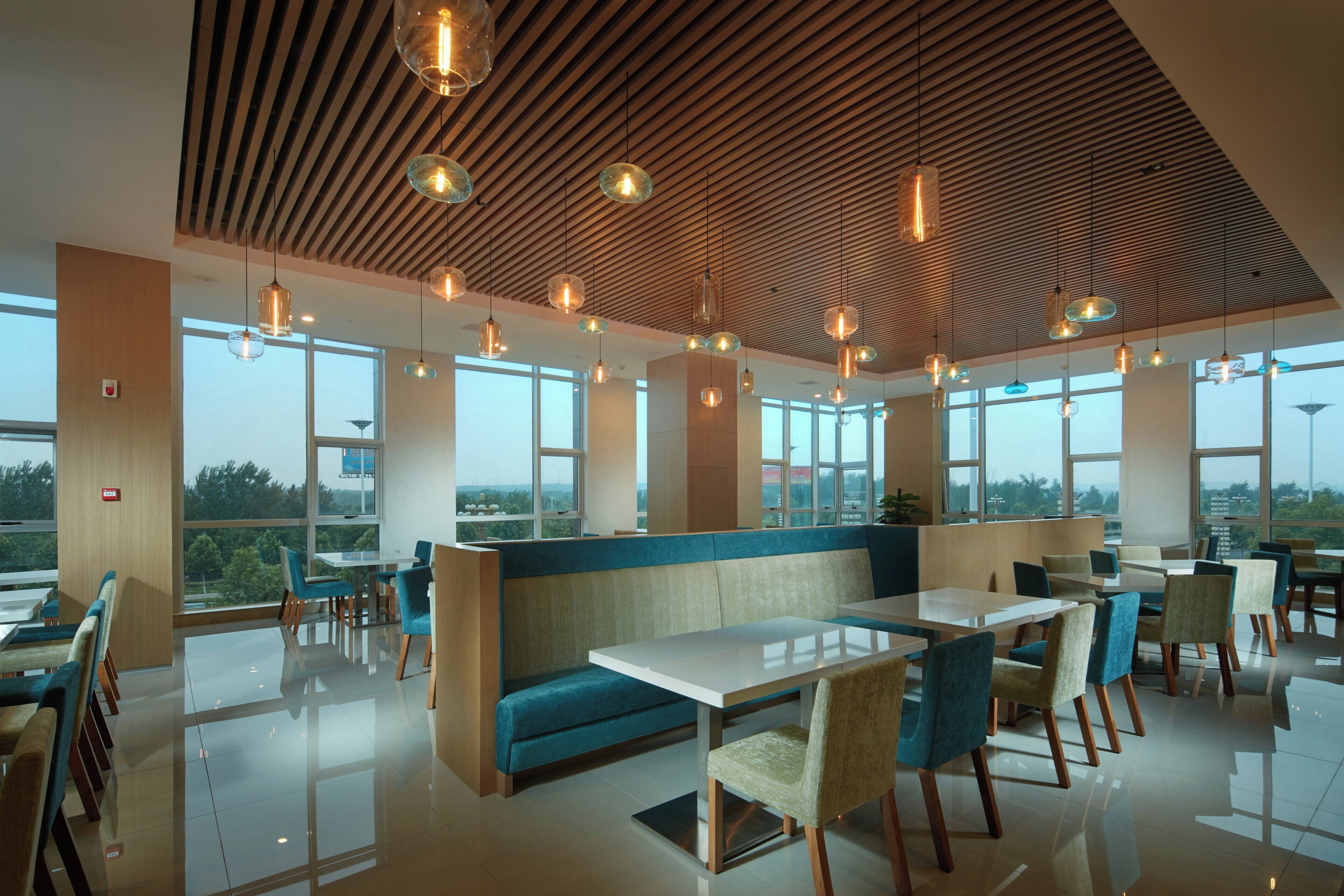 A modern dining area with a wooden ceiling, large windows, and a mix of seating arrangements including tables and booths.