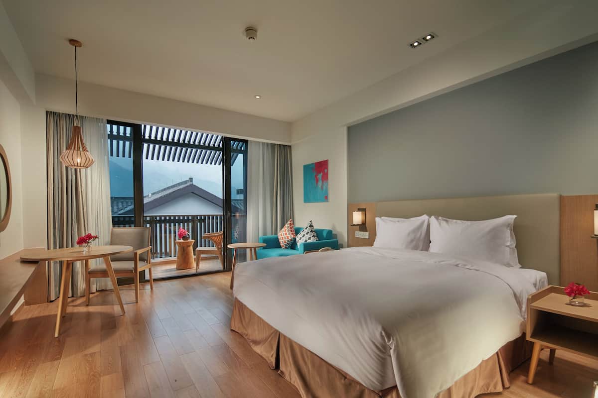 Ein Hotelzimmer mit einem großen Bett, einem Holztisch, einer Couch und einem Balkon mit Blick.