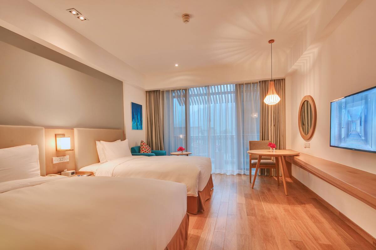 Ein Hotelzimmer mit zwei Betten, einem Schreibtisch, einem Stuhl, einem Fernseher und einem Fenster mit Vorhängen.