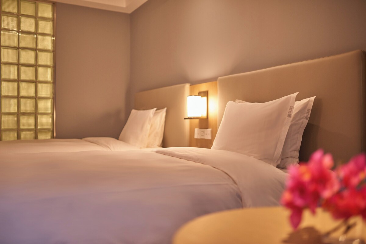 A hotel room with a large bed, a nightstand with a lamp, and a window with a view.