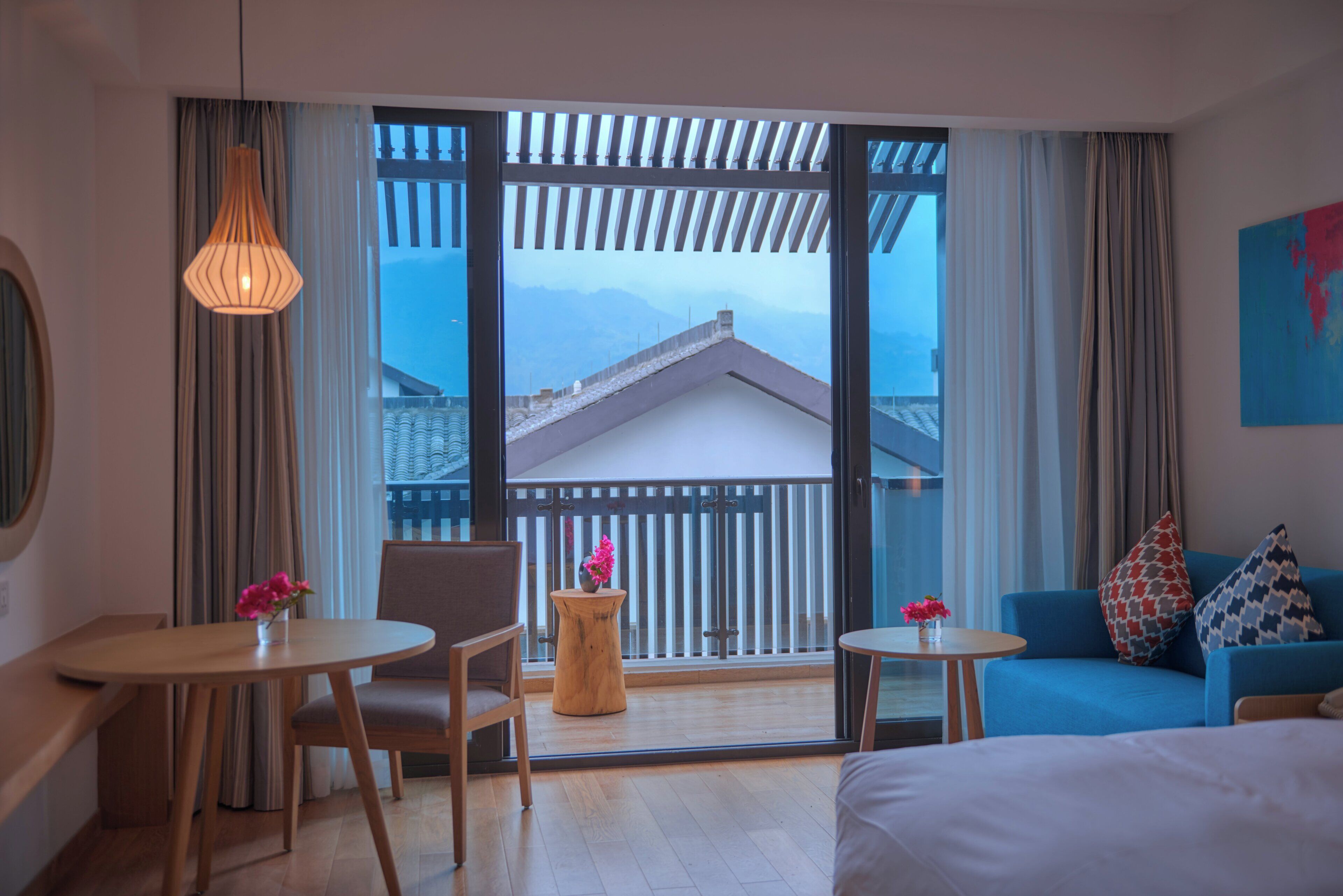 A hotel room with a balcony, a bed, a sofa, two tables, and a chair.