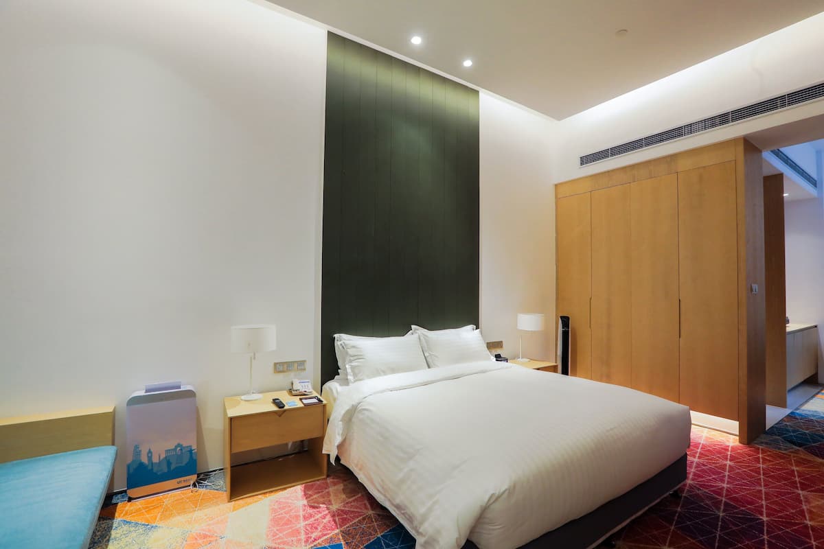 A modern hotel room with a large bed, a nightstand, a desk, and a wardrobe.