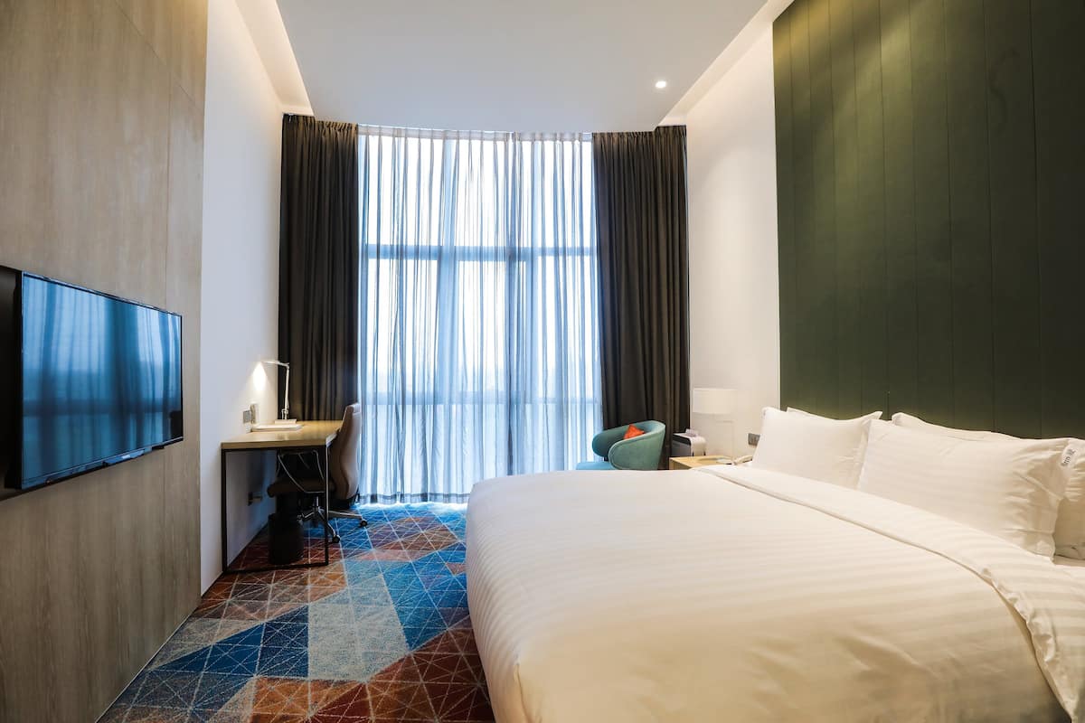 A hotel room with a bed, a desk, a chair, a TV, and a window with curtains.