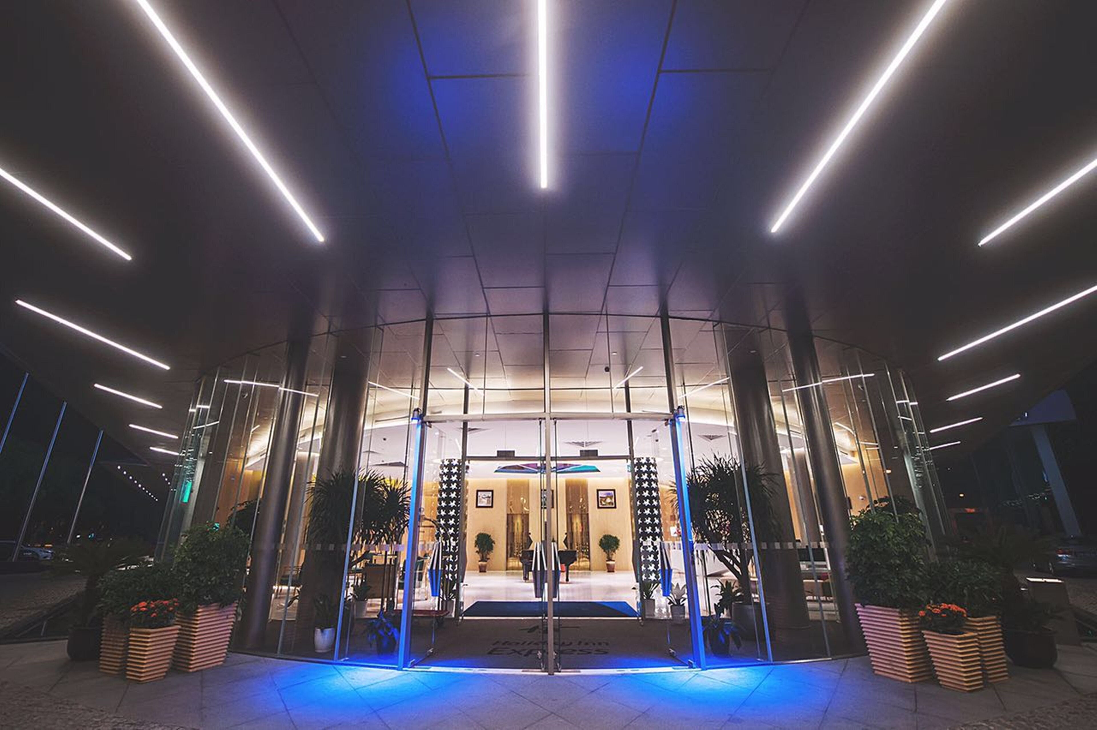 En modern hotellentrél med en glasfasad, upplyst av belysning ovanifrån.