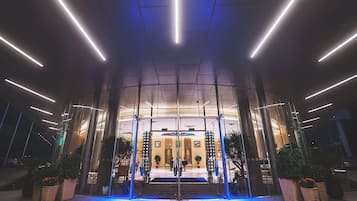 En modern hotellentrél med en glasfasad, upplyst av belysning ovanifrån.