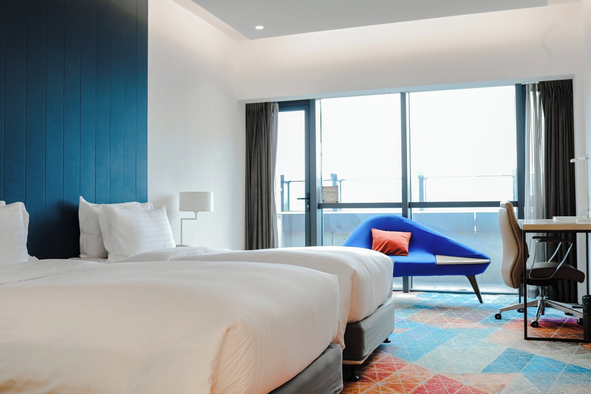 A hotel room with a large bed, a desk, a chair, and a view of the outdoors.