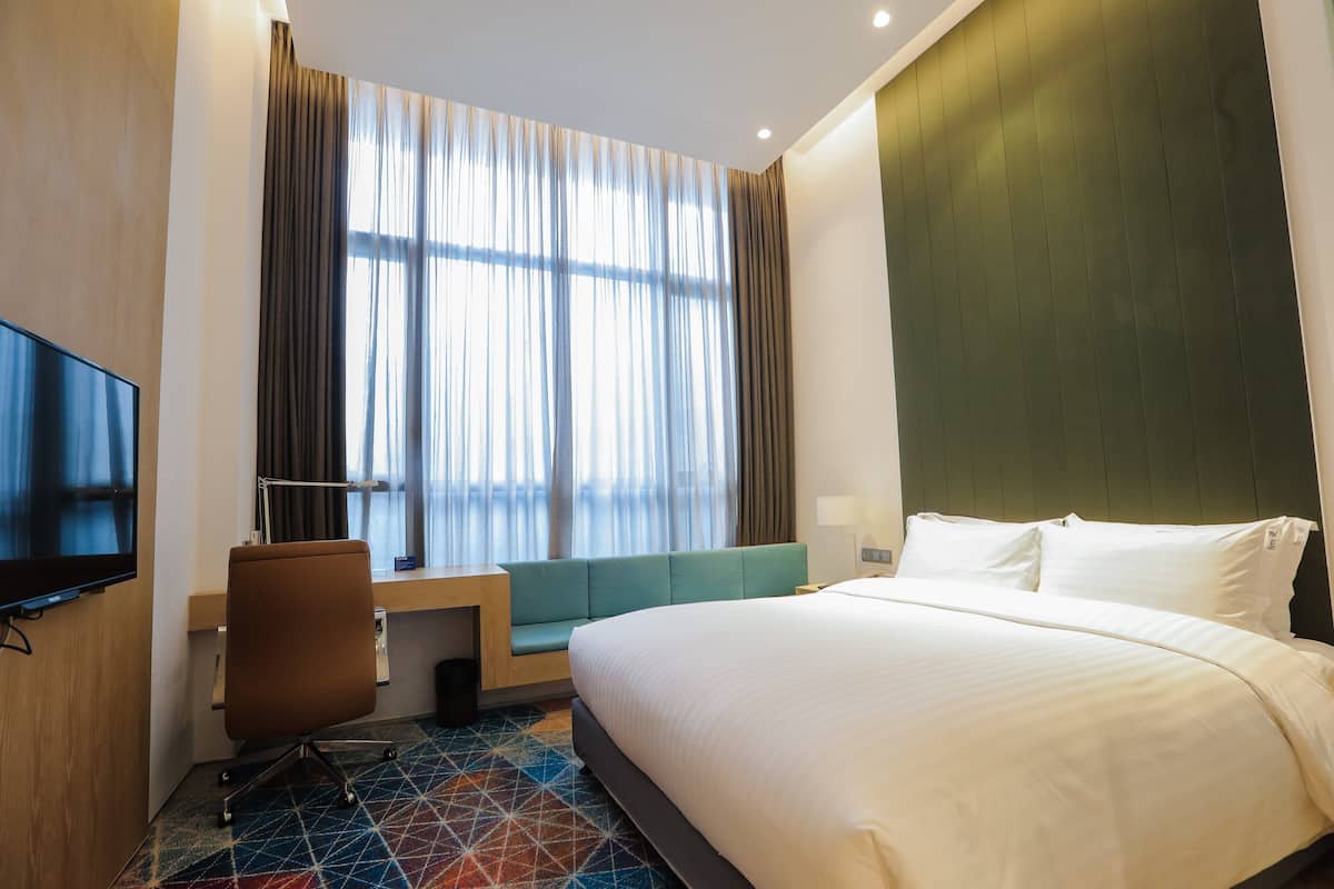 A hotel room with a large bed, a desk with a chair, a television, and a window with curtains.