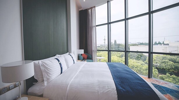Une chambre d’hôtel dotée d’un grand lit, offrant une vue sur la verdure et les bâtiments par la fenêtre, et présentant un design moderne.