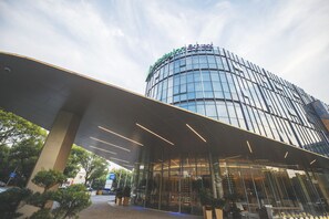 Un hôtel moderne doté d’une façade en verre incurvée et d’une entrée imposante surmontée d’un auvent.