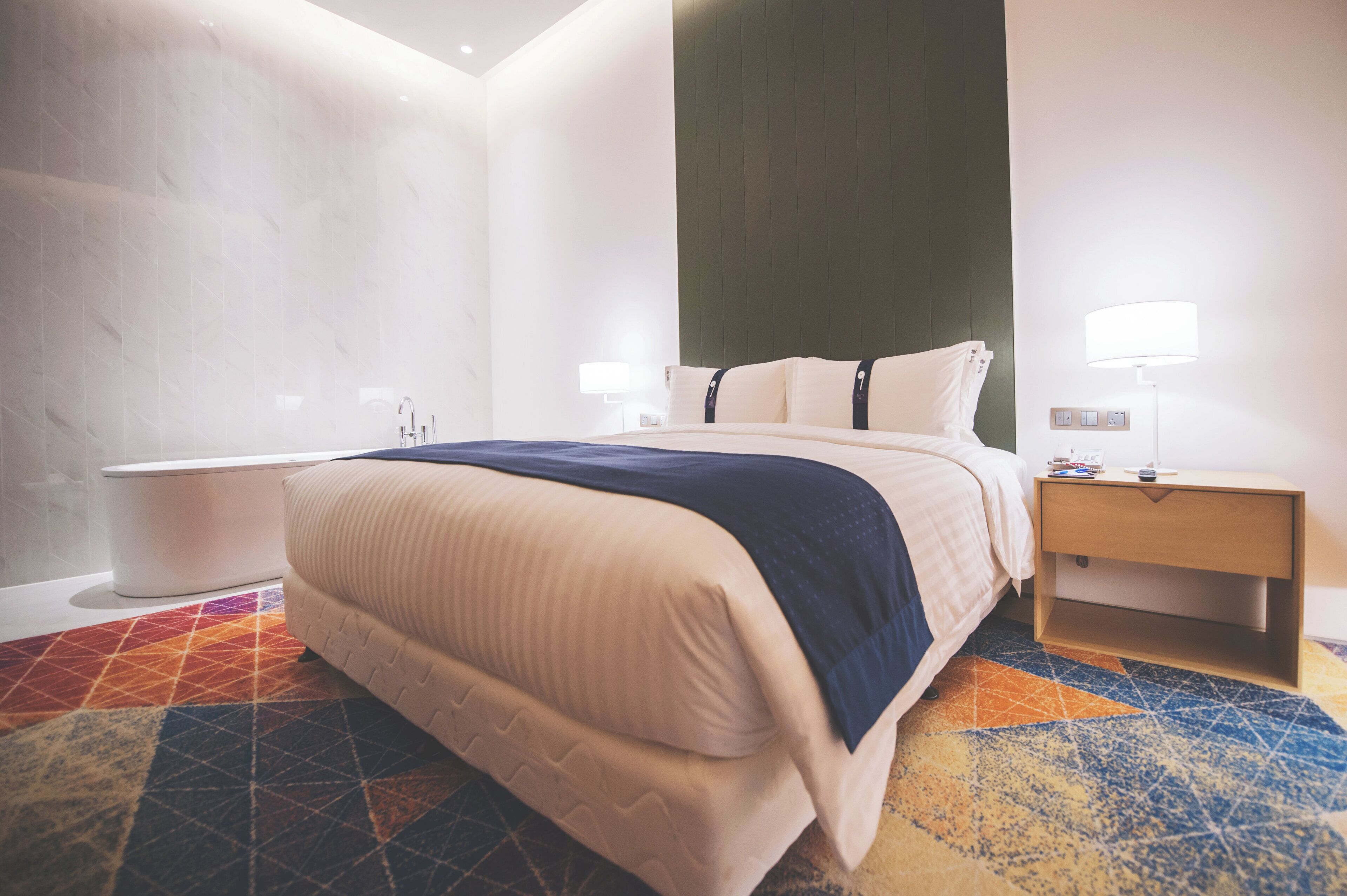 A hotel room with a bed, bedside table, lamp, and a bathroom with a toilet and sink.