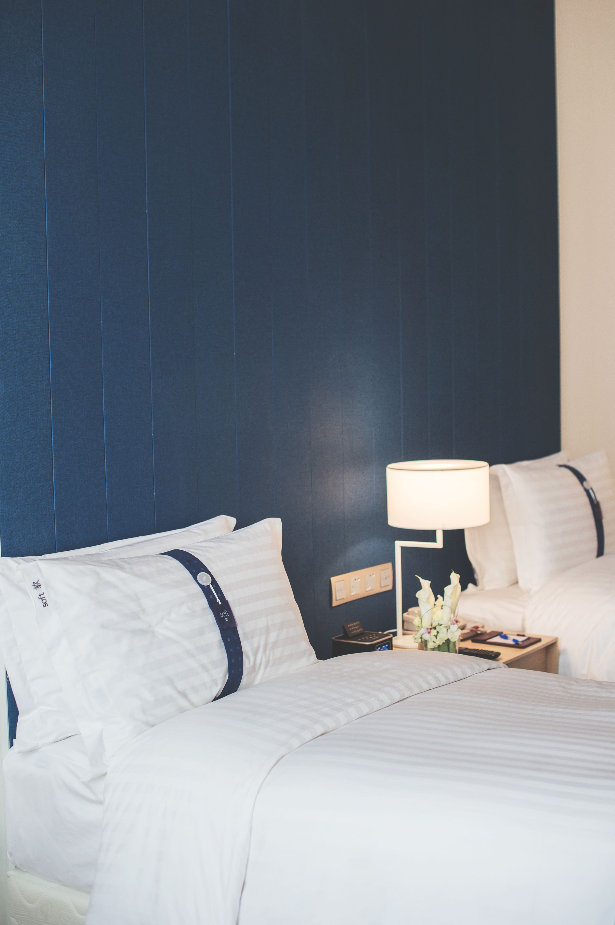 A hotel room with a large bed, a bedside table with a lamp, and a nightstand with a vase of flowers.