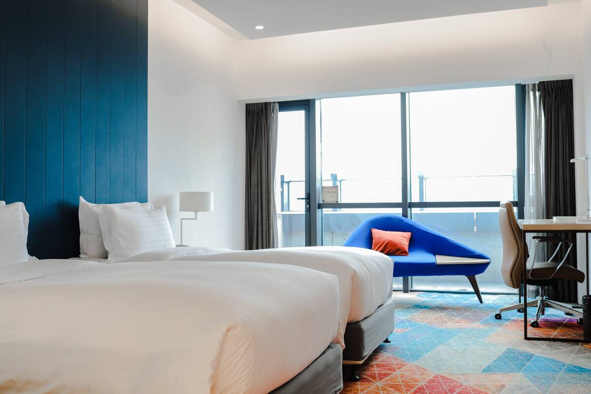 A hotel room with a large bed, a desk, a chair, and a balcony view.