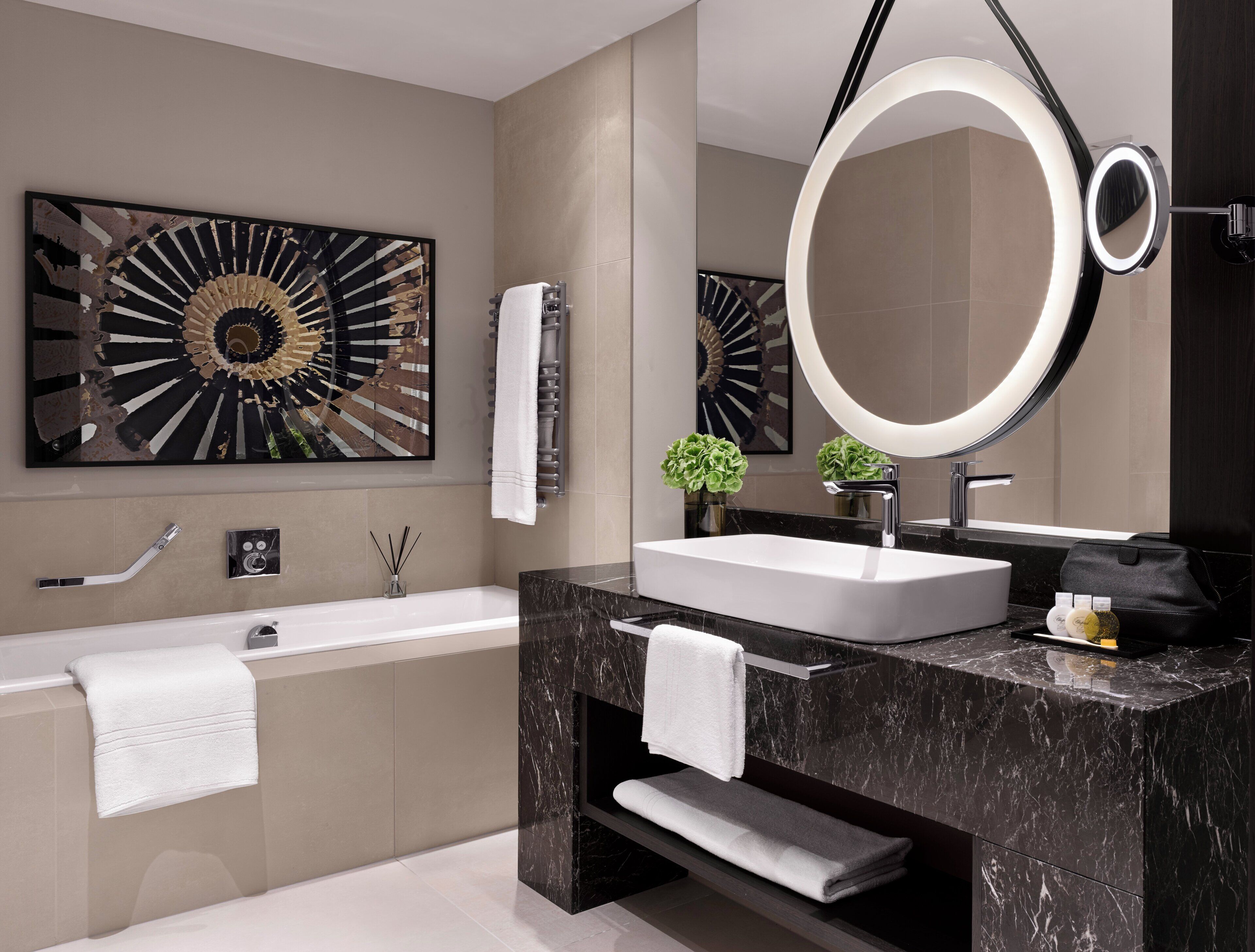 Un baño moderno con un espejo grande, una bañera, un tocador con lavabo y un adorno en la pared.
