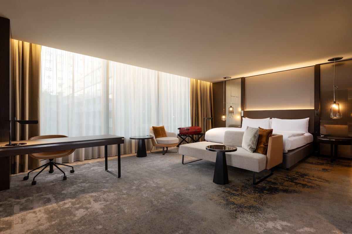 Een moderne hotelkamer met een bed, bureau, stoel en een groot raam met gordijnen.