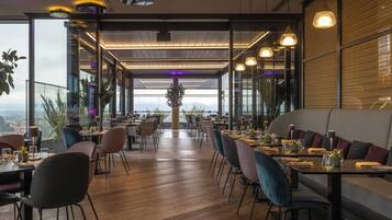Um restaurante moderno com teto alto, piso de madeira e diversas opções de assentos, incluindo mesas e cabines.