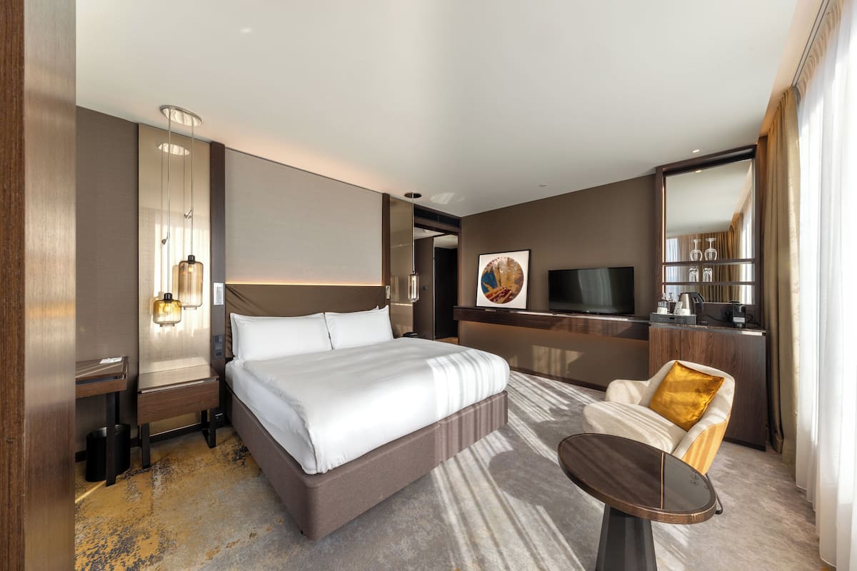 Een moderne hotelkamer met een groot bed, een bureau, een stoel, een klein tafeltje en een televisie.