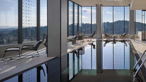 Un área de piscina interior moderna con amplias ventanas, asientos y vistas a la ciudad.