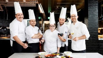 Un grupo de chefs en una cocina moderna con encimeras de mármol y paredes de ladrillo negro.