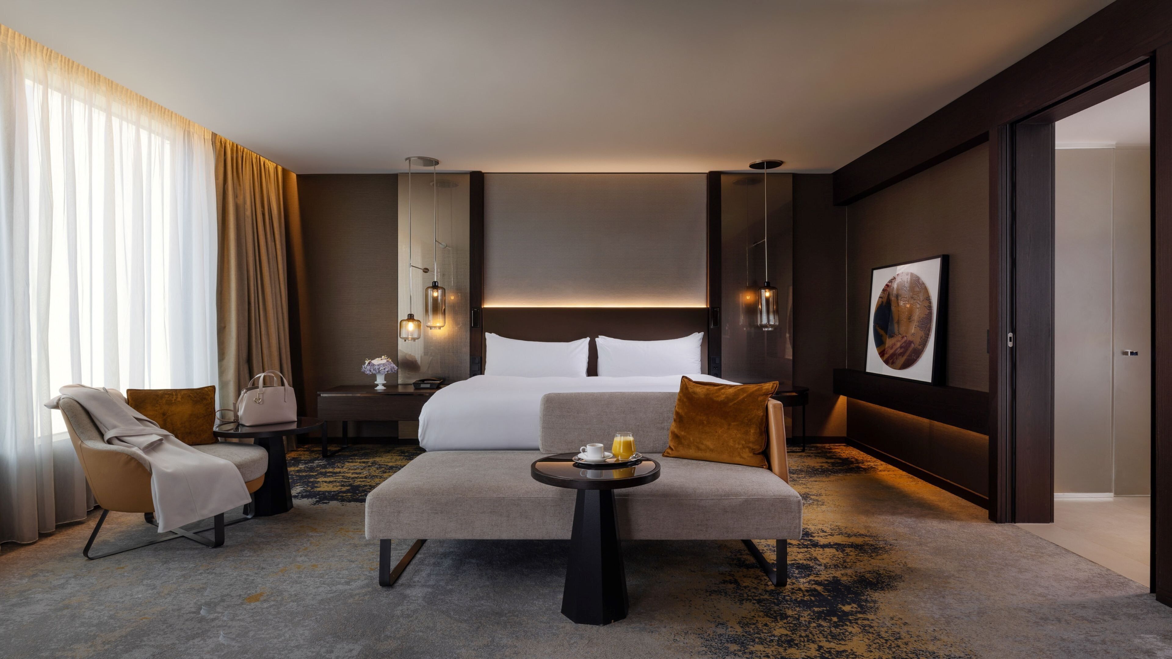Une chambre d’hôtel moderne dotée d’un grand lit, d’un coin salon avec une table et offrant une vue sur la ville par la fenêtre.