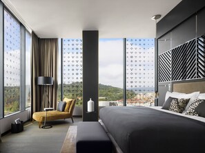 Une chambre d’hôtel moderne dotée d’un grand lit, d’un canapé, d’un lampadaire et offrant une vue sur le paysage urbain grâce à de grandes fenêtres du sol au plafond.