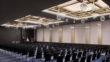 A conference room with rows of chairs, a stage, and a ceiling with hanging spherical light fixtures.